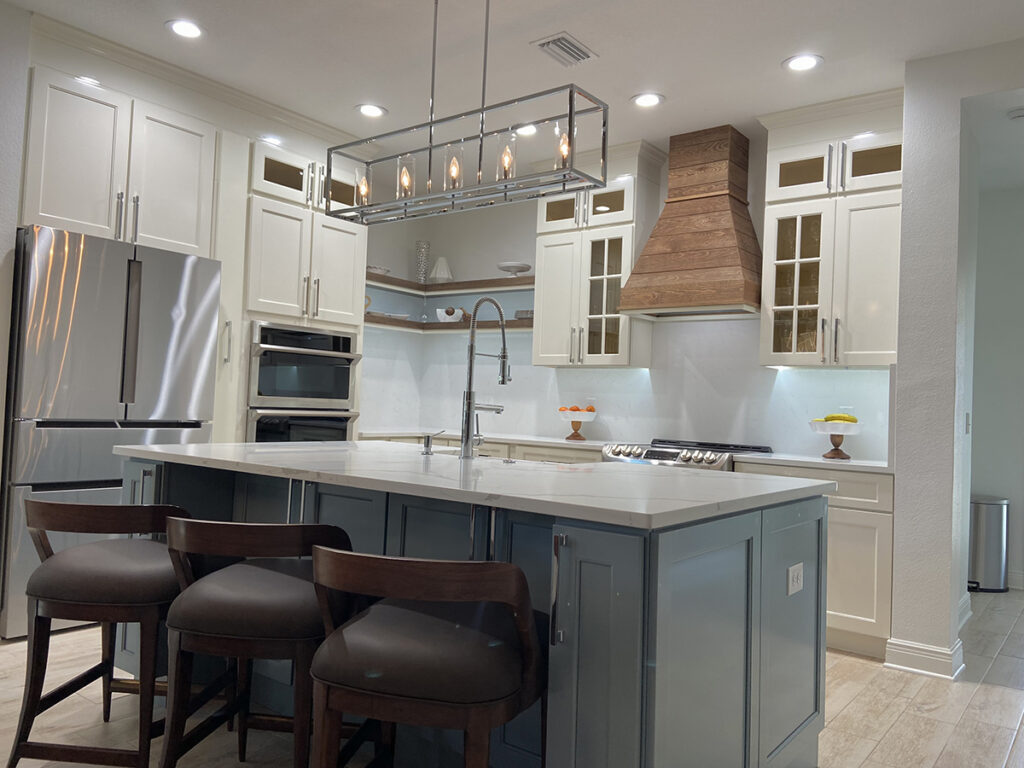 A remodeled home in St. Petersburg, designed by Edwin Ambert Interiors. kitchen redesigned to make more space. The new layout features a double oven, along with a custom hood over the stove top. The island was also expanded to give more counter space, and painted with a complimentary color to stand out from the rest of the kitchen.